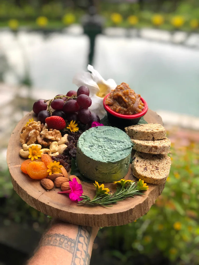 A living-food cheese board with crackers, fruit, nuts, and flowers beside the pool