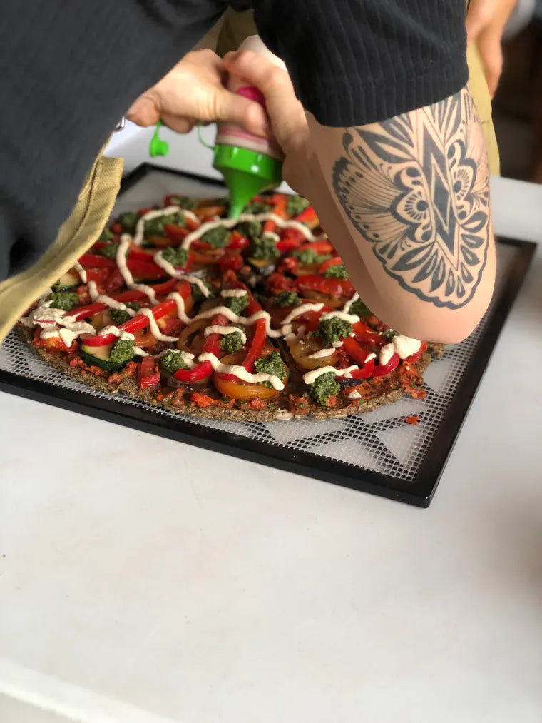 A student adding the final sauce to a colourful raw pizza