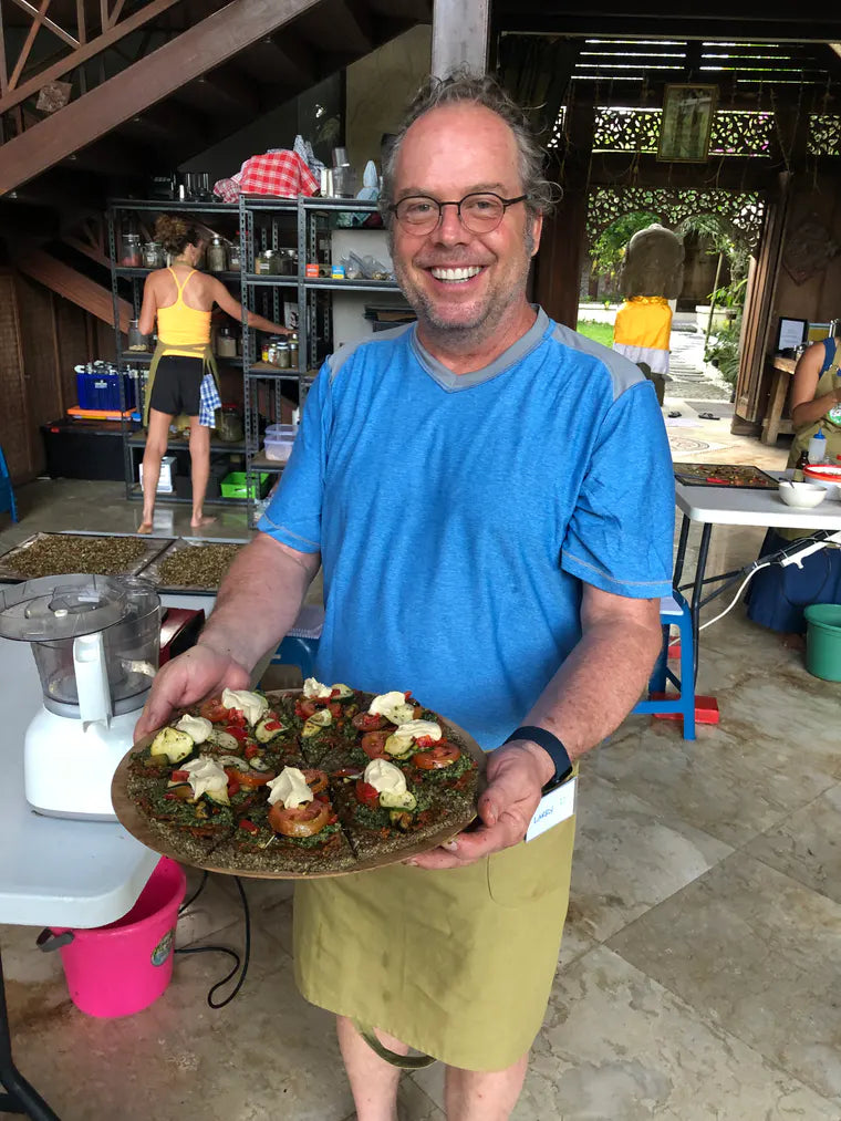 A smiling student proudly presenting a finished raw pizza